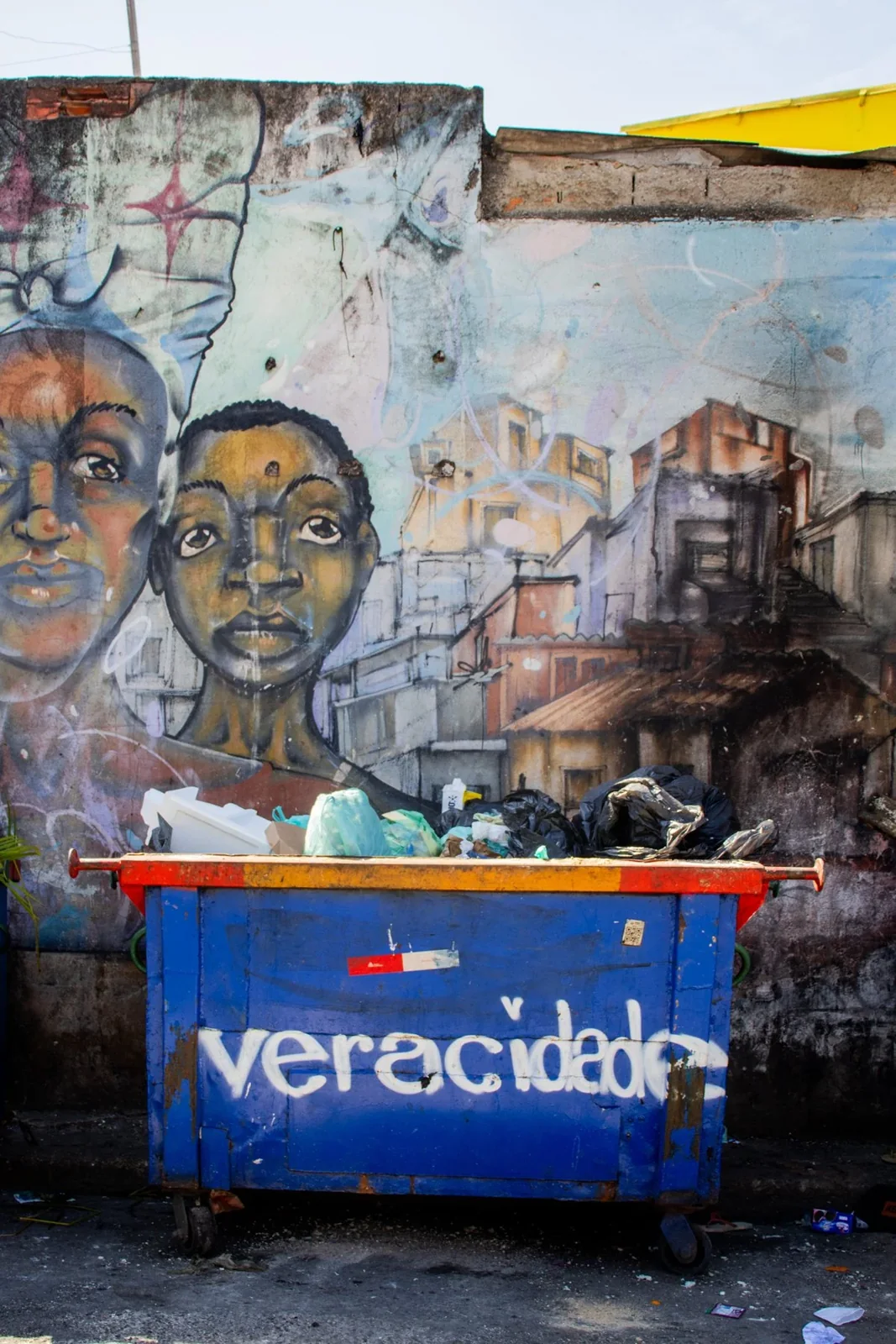 Parede pintada com retratos, portão e elementos do cotidiano urbano