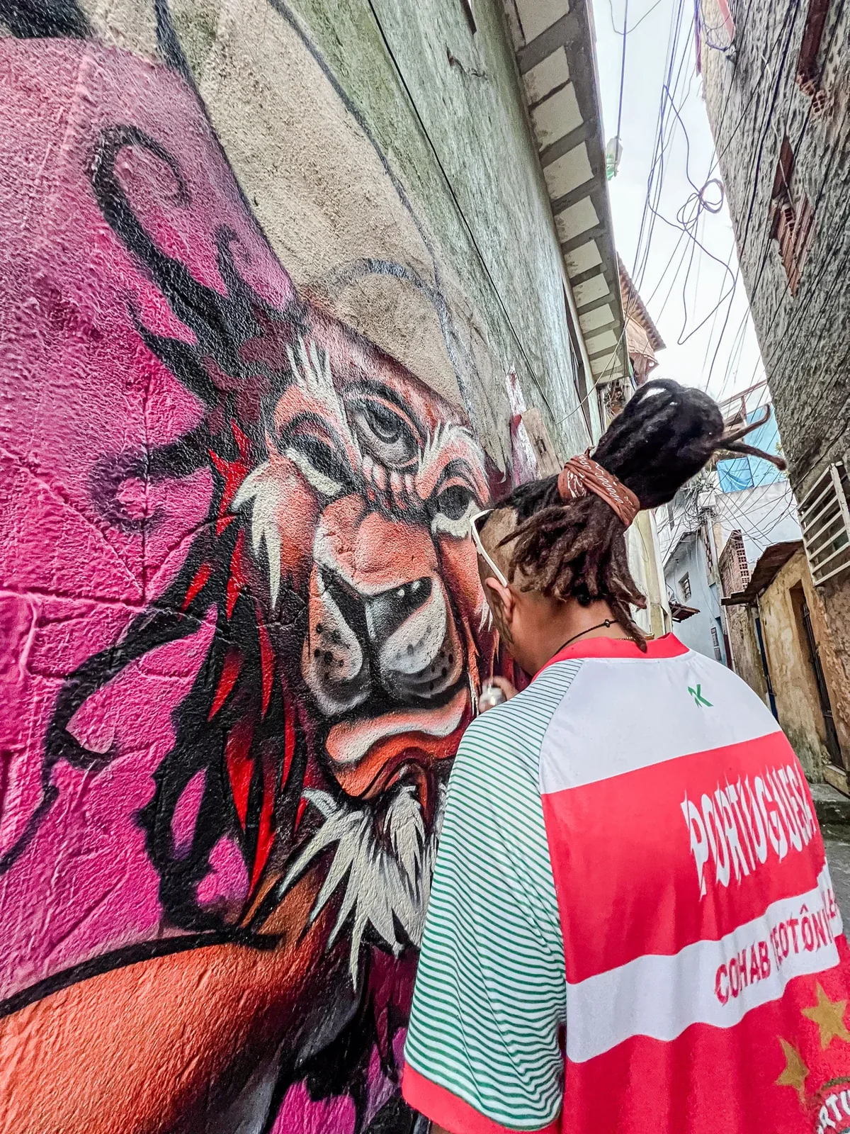 Artista com tranças pinta personagem de expressão intensa em muro rosa