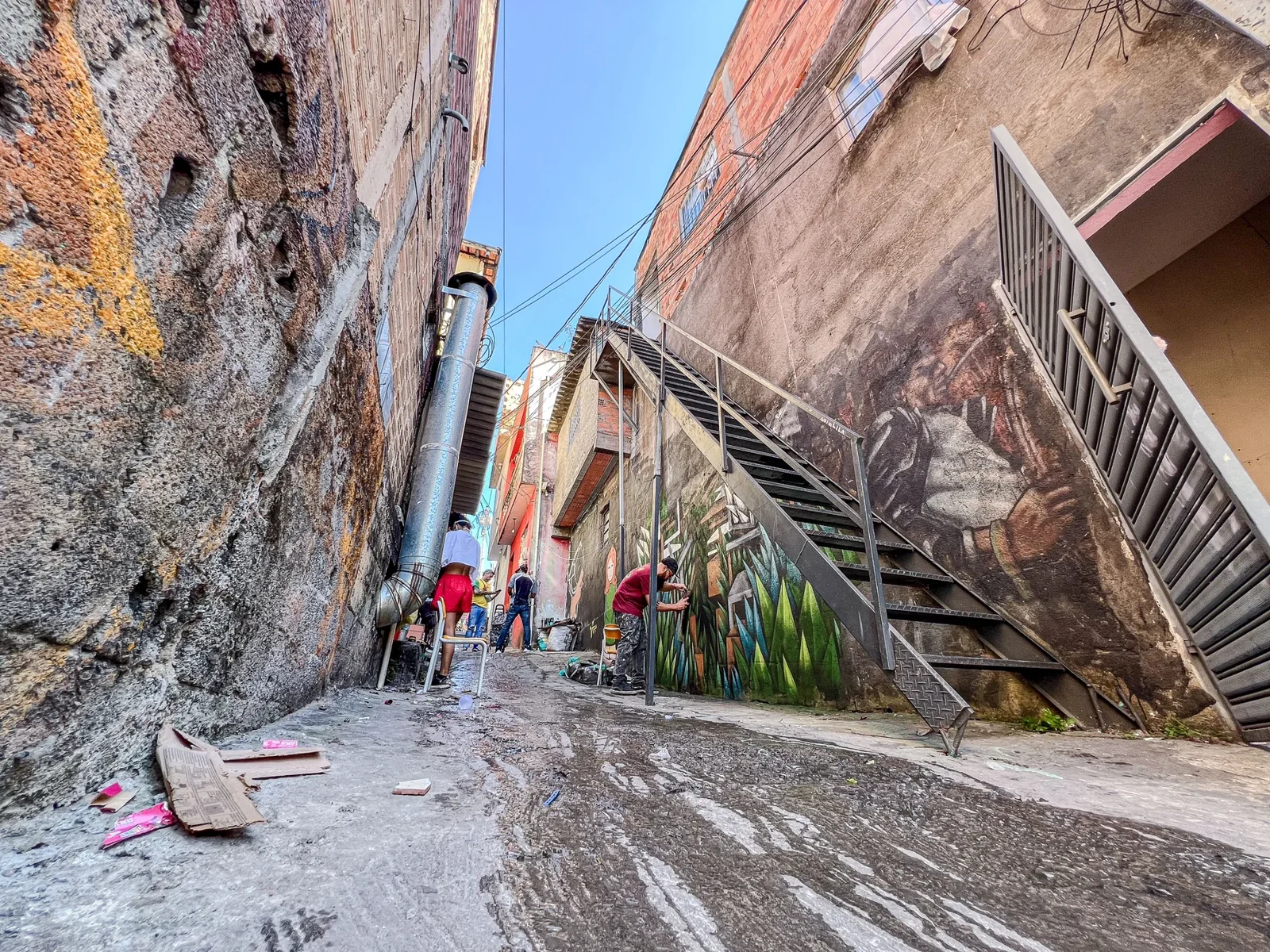 Passagem entre fachadas pintadas, com escada ao lado das casas