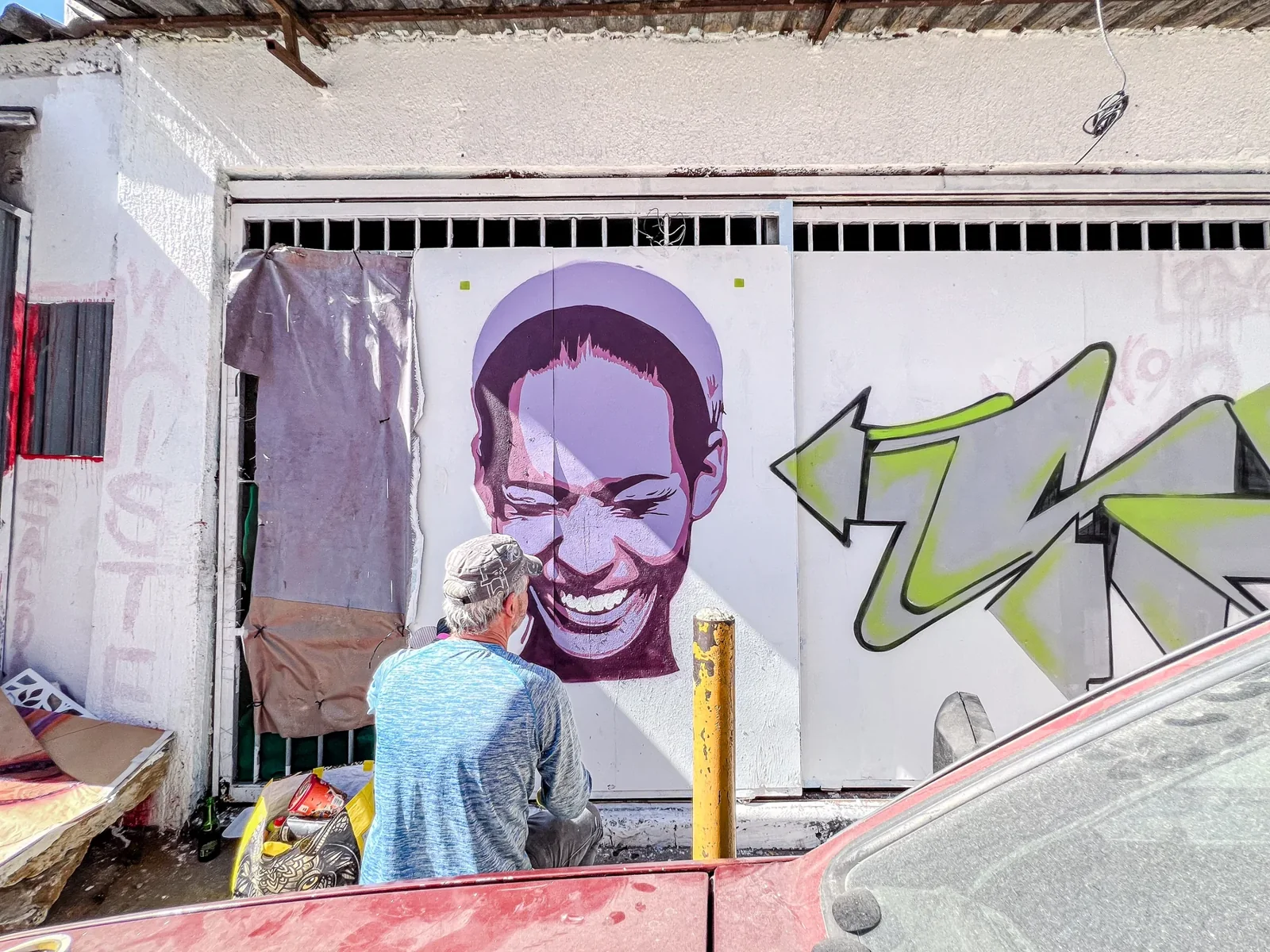 Artista desenvolve um retrato em tons roxos sobre parede de rua