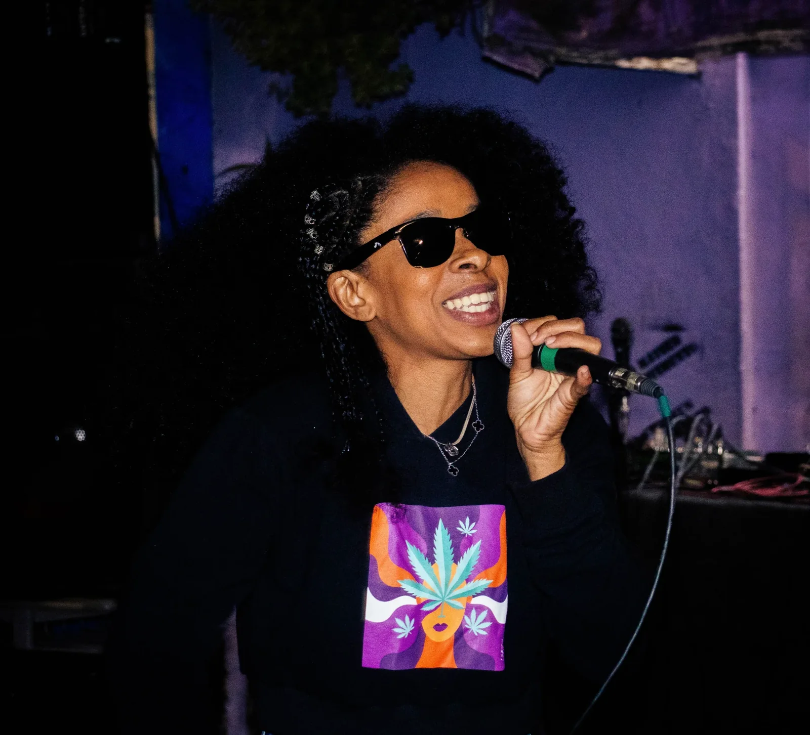 Cantora se apresenta com microfone diante de iluminação colorida
